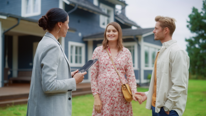 Portrait of a Happy Young Couple with Pregnant Female Talking with a Realtor, Interested in Renting or Buying a New Home. Real Estate Agent Talking With Clients In Front of the House. Royalty-Free Stock Footage #1097187927