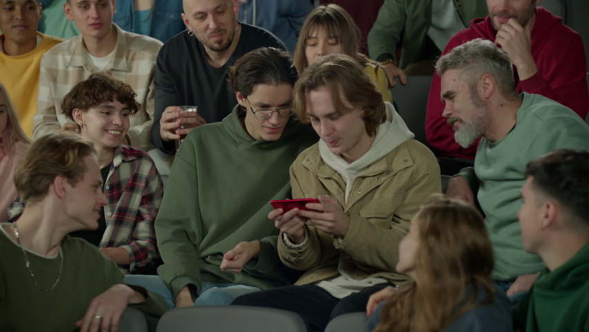 Audience sits at sports event, looking into the phone screen of a spectator instead of the game | Shutterstock HD Video #1097189831