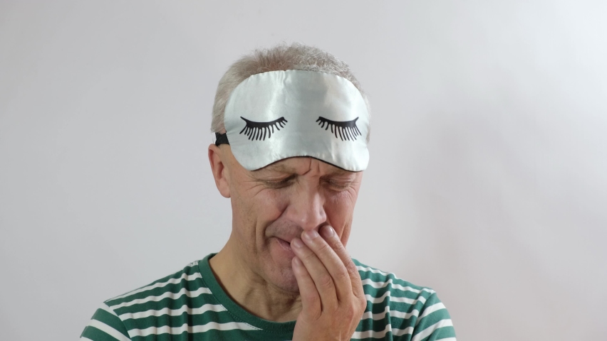 Bearded man in sleep mask feeling tired, gray studio background. Concept of insomnia, dreams and relaxation insomnia in the elderly | Shutterstock HD Video #1097190583