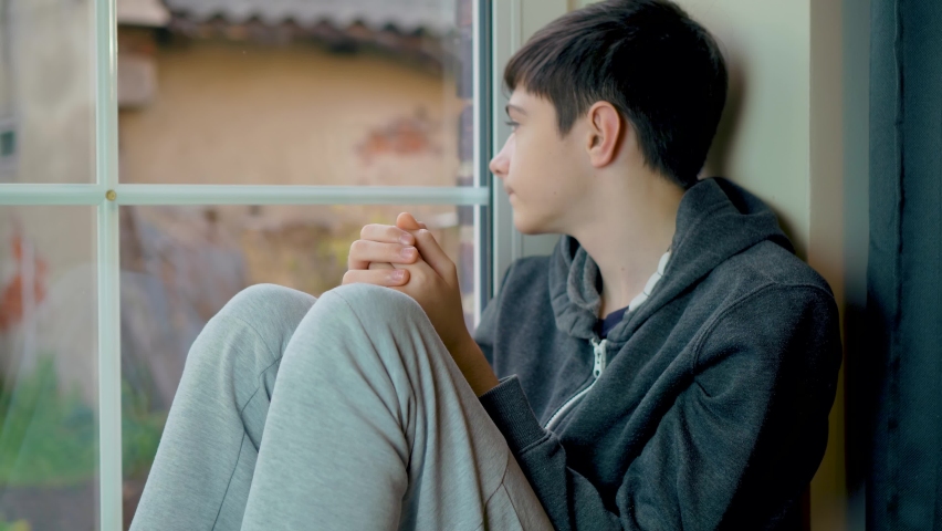 Sad boy refugee from Ukraine sitting looking through window and cannot go outside home because Russian military invasion. Save lifes, no war, world peace, stop conflict, born love. Childhood in | Shutterstock HD Video #1097192509
