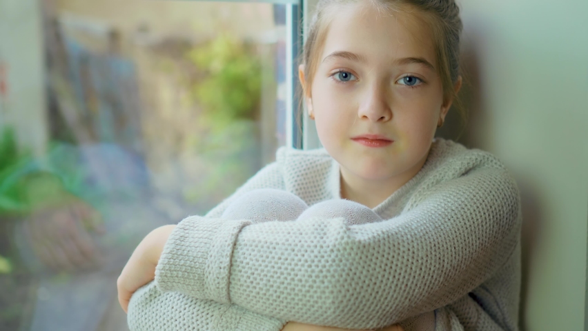 Portrait of cute girl looking in camera near window, thinking about something. Happy carefree childhood concept | Shutterstock HD Video #1097192517