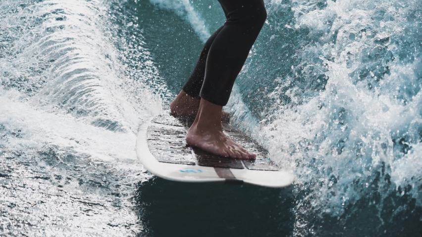 Wakesurfing on the river. Wakesurfer in a wetsuit. Goofy stance. Water sport. Close-up of the wakeboard and the wakesurfer's legs. 4К