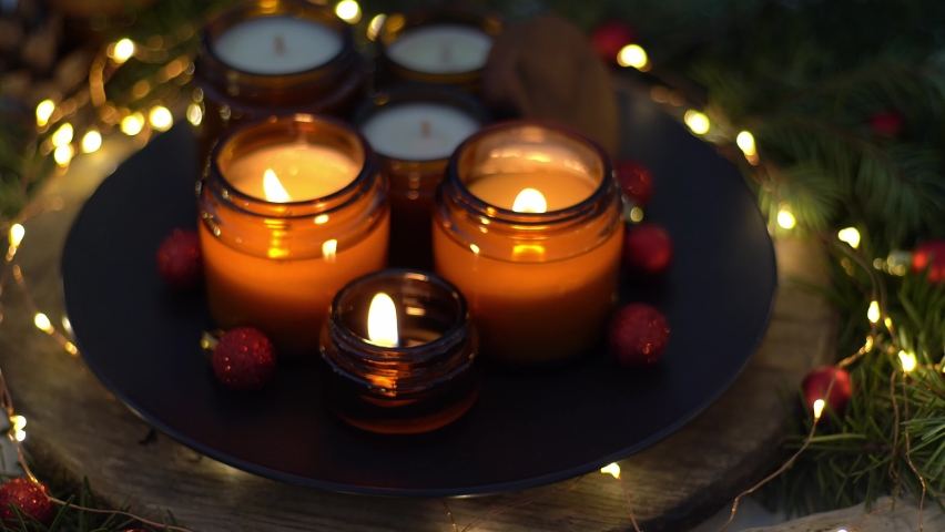 Soy candles burn in glass jars. Comfort at home. Candle in a brown jar. Scent and light. Scented handmade candle. Aroma therapy. Christmas tree and winter mood. Cozy home decor. Red balls decoration Royalty-Free Stock Footage #1097194541