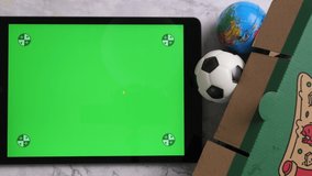 Top view of tablet with green screen display, pizza and balls on the table.
