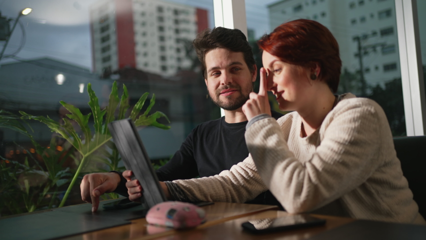 Young woman telling I told you so to boyfriend sitting at coffee shop. Couple at cafe looking at tablet device screen