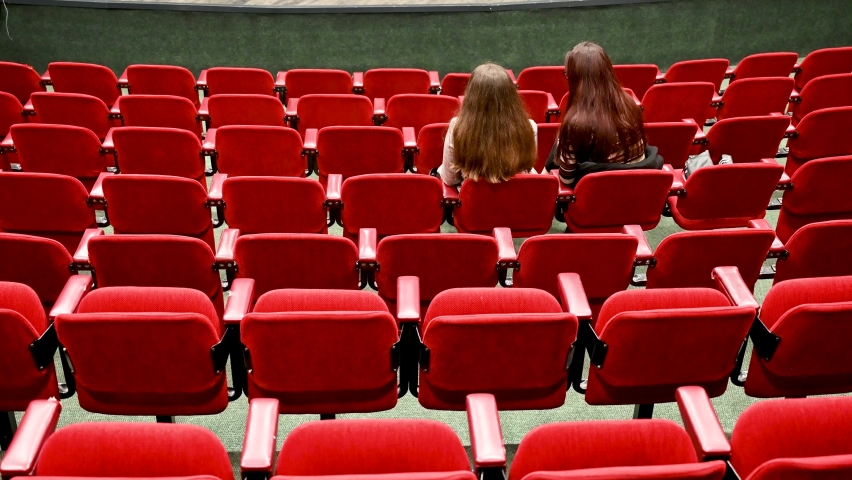 Two girls sitting in cinema. Red chairs in cinema. Rows of chairs in theatre.  Royalty-Free Stock Footage #1097197671