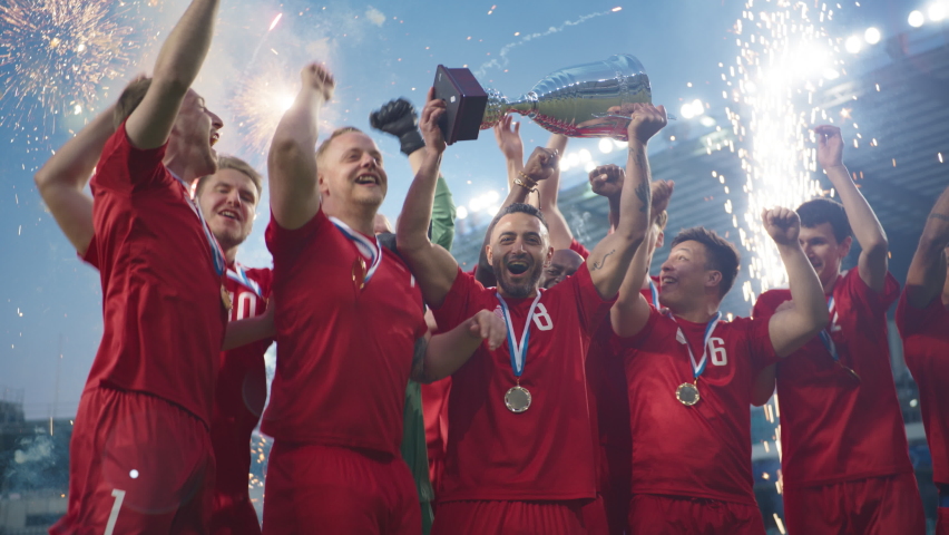 Football Finals Tournament Winning Team Celebrates Victory Cheering and Lifting Trophy Prize on Stadium. Happy Soccer Players Champions of International Championship Cup. Slow Motion Fireworks Shot