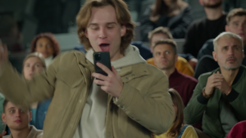 Caucasian male can't control his emotions after winning a bet on his phone during a sport event. Television like camera zoom