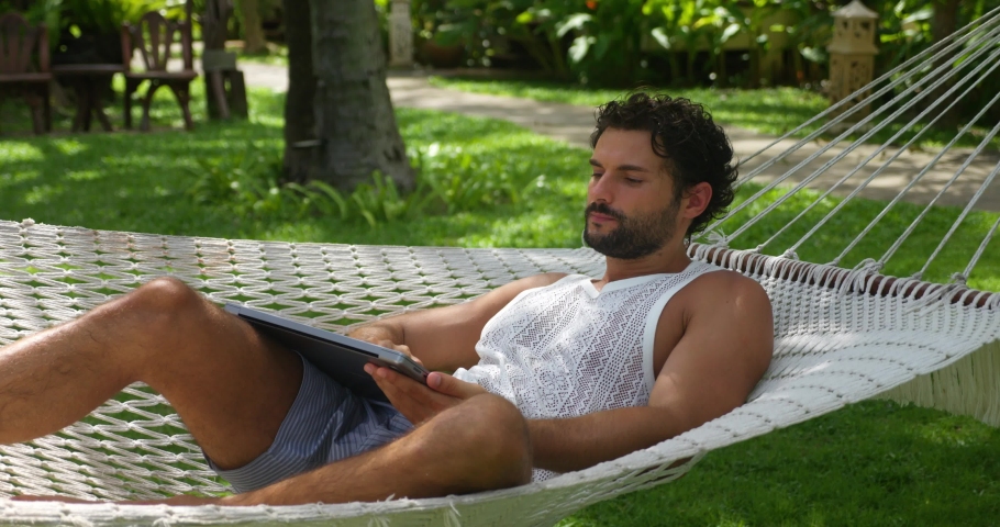 Successful man developer, programmer turns on laptop while chilling in a hammock, telecommuting on vacations. Freelancer working remotely from coastal resort, planning new project in quite atmosphere