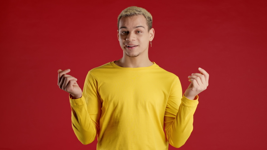 Smiling man pointing down to advertising area. Red background. Young teenager asking to click to subscribe below. Copy space for your commercial idea, promotional content. | Shutterstock HD Video #1097208103