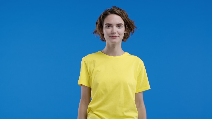 Smiling woman pointing down to advertising area. Blue background. Young lady asking to click to subscribe below. Copy space for your commercial idea, promotional text content. | Shutterstock HD Video #1097208111