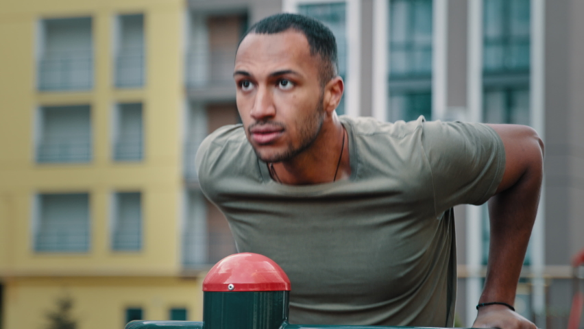 Healthy bodybuilder sportsman latino african man athlete professional trainer doing sport exercises outdoors on city gym pushing ups muscular male body on bars training arm muscles sporting activity