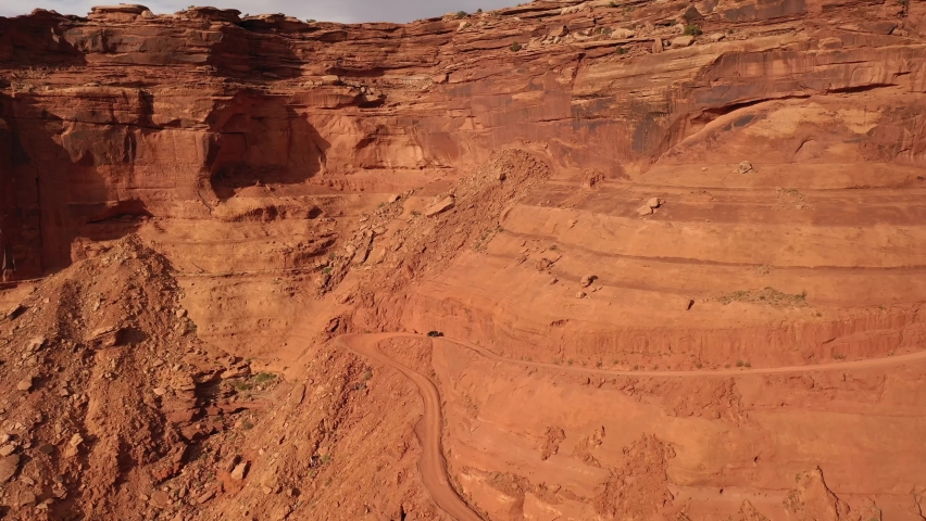 A black jeep drive around an S curve while navigating down the orange cliffs in the canyons of Utah in late afternoon sun.