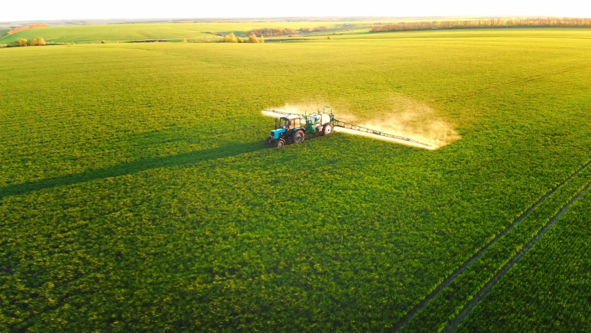 Aerial footage. Pesticide Sprayer Tractor working on a large green field at sunset. Aerial shot following on the side a tractor spraying wheat field against diseases. Farmer spraying soybean fields. Royalty-Free Stock Footage #1097218173