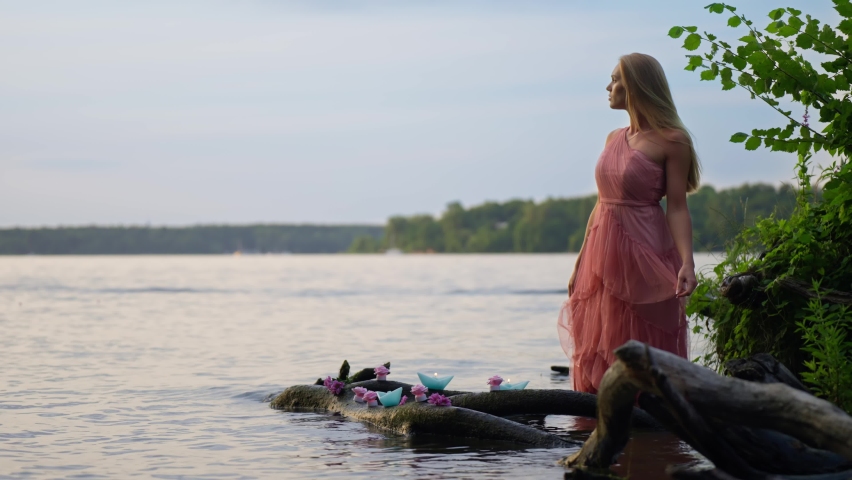 A gorgeous blonde woman wearing a pink dress in the water next to candles and flowers