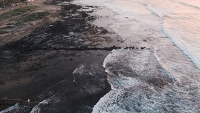 Aerial view of the waves crashing on the rocky shoreline at sunset. Playa de Las Americas, Tenerife. High quality video.