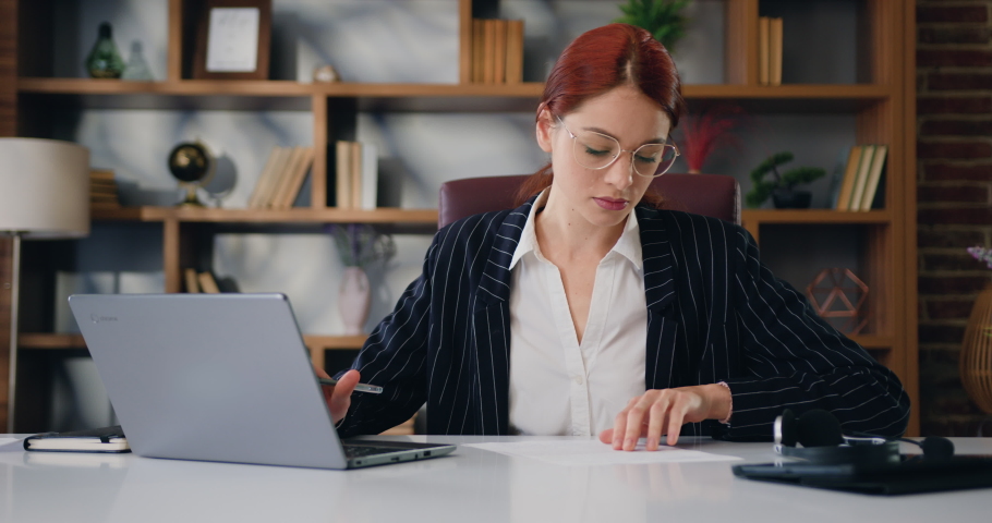 Caucasian young woman calculates expenses, income, estimates project budget, accountant conducts financial audit, summarizes the total amount using a laptop program at modern office Royalty-Free Stock Footage #1097223323