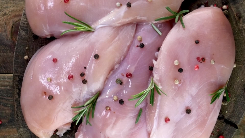 Fresh raw chicken breast fillets sprinkled with peppercorns and rosemary on round wooden board rotates slowly. Top view. Royalty-Free Stock Footage #1097225135