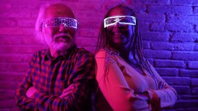 Happy elderly friends having fun with futuristic augmented reality glasses, multiracial couple Asian male and Hispanic American female - Metaverse Concept