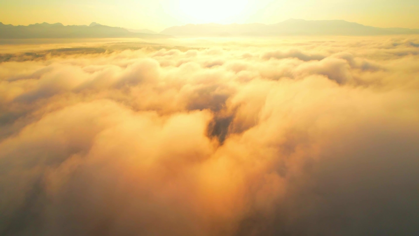 Aerial view from a drone flying over heavy dense fog during sunrise, Mountain scenery and sky in the background. amazing scenery in golden hour. Chiang Mai, Northern Thailand. 4K. nature concept
