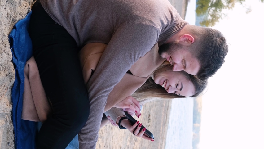 Young man and woman sitting on the beach and looking at the phone