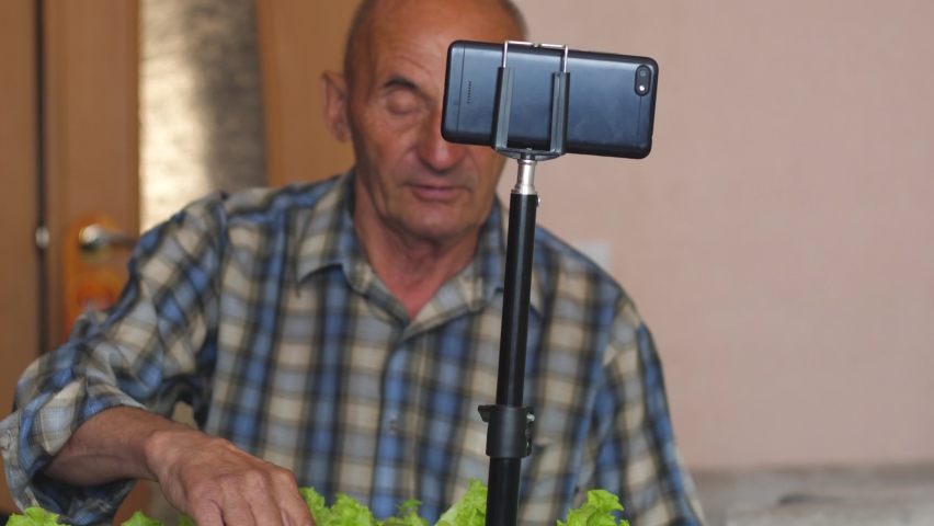 Active peppy pensioner 70-75 years old shoots a blog for social networks sitting in front of a smartphone camera on a tripod. an elderly man streams about his hobby growing houseplants
 | Shutterstock HD Video #1097229377