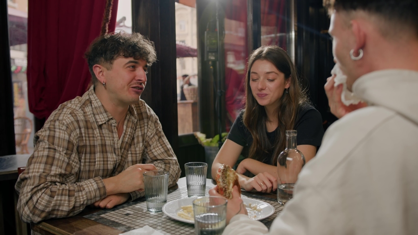 Wide shot - a group of friends chatting at a table in a restaurant, eating burger and french fries | Shutterstock HD Video #1097231345