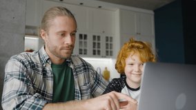 Smiling father and kid talk by video call. Man hugs preschooler boy shoulders and points finger to screen. Happy bearded man talks gesturing emotionally closeup