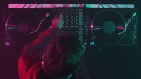 Hip hop DJ mixing vinyl records on turntables in night club. Disc jockey plays set in overhead video clip