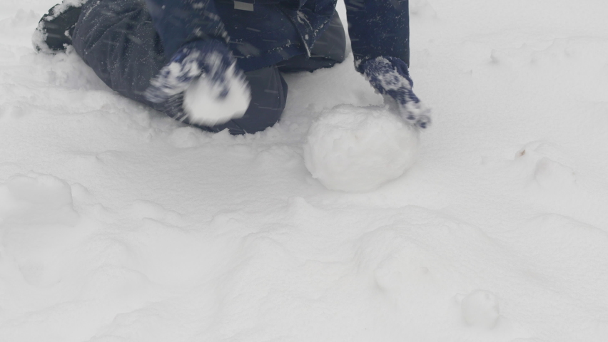 A child in winter gloves sculpts a snowman from fresh snow crawling on his knees. christmas snowfall, children play in the snow. winter holidays, children celebrate new year | Shutterstock HD Video #1097234413