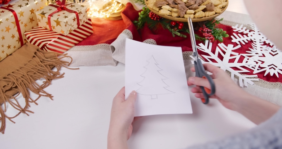 The girl cuts out decorations from paper for Christmas and New Year. DIY decorations on the background of the Christmas table with gifts. High quality 4k footage | Shutterstock HD Video #1097235461