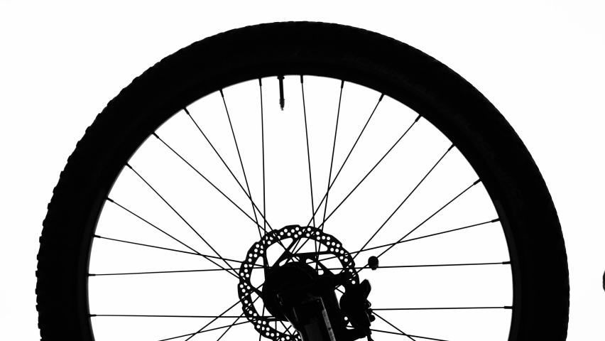 Black silhouette of a bicycle wheel spinning on a white isolated background. Close up of round bike wheel with rubber tread tire, spokes and brake. Rotation of the wheel on a sporty modern bike.