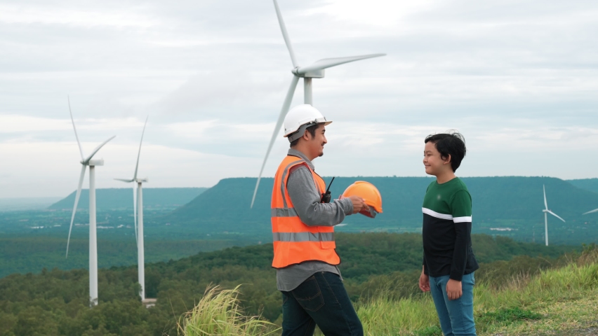 Engineer with his son on a wind farm atop a hill or mountain in the rural. Progressive ideal for the future production of renewable, sustainable energy. Energy generation from wind turbine. | Shutterstock HD Video #1097240983