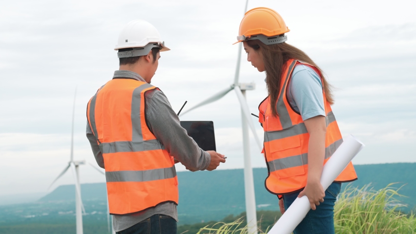 Male and female engineers working on a wind farm atop a hill or mountain in the rural. Progressive ideal for the future production of renewable, sustainable energy. | Shutterstock HD Video #1097241009