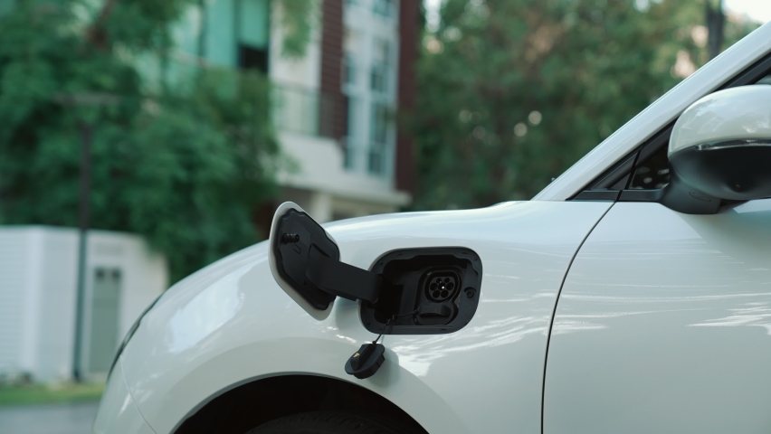 Progressive woman installs a charging station plug into her electric vehicle at home. EV automobiles provide an environmentally beneficial concept of clean and green energy. | Shutterstock HD Video #1097241025
