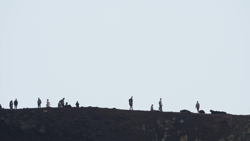 Tourists hiking through volcanic Mount Etna. People enjoying adventurous vacation at famous place. View of dramatic landscape with sky covered in smoke in background. Climbing mount Etna.