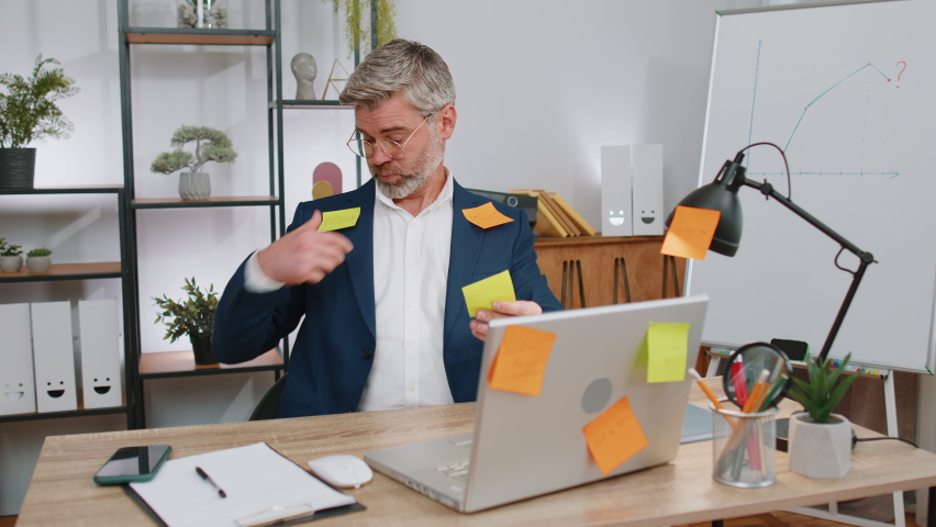 Tired exhausted mature businessman working on laptop at office with many sticker task inscriptions. Freelancer old man busy occupation feels sad boredom overworked multitasking. Panic attack, deadline | Shutterstock HD Video #1097242557