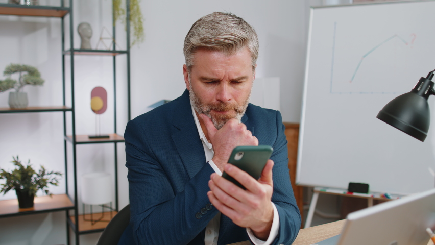 Mature businessman in suit use smartphone typing browsing, loses becoming surprised sudden lottery results, bad news, fortune loss fail at home office desk workplace. Middle aged freelancer worker man | Shutterstock HD Video #1097242601