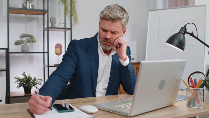 Stressed mature man feeling worried about problem analyzing information, read business papers prepare financial report at office. Freelancer frustrated thinking of money debt, budget loss bankruptcy | Shutterstock HD Video #1097242617
