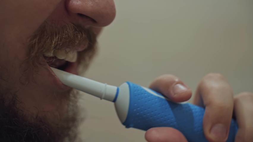 Man brushes his teeth with an electric toothbrush. Daily routine procedure for health. Thick mustache and beard on a male's face. Oral hygiene. | Shutterstock HD Video #1097245977