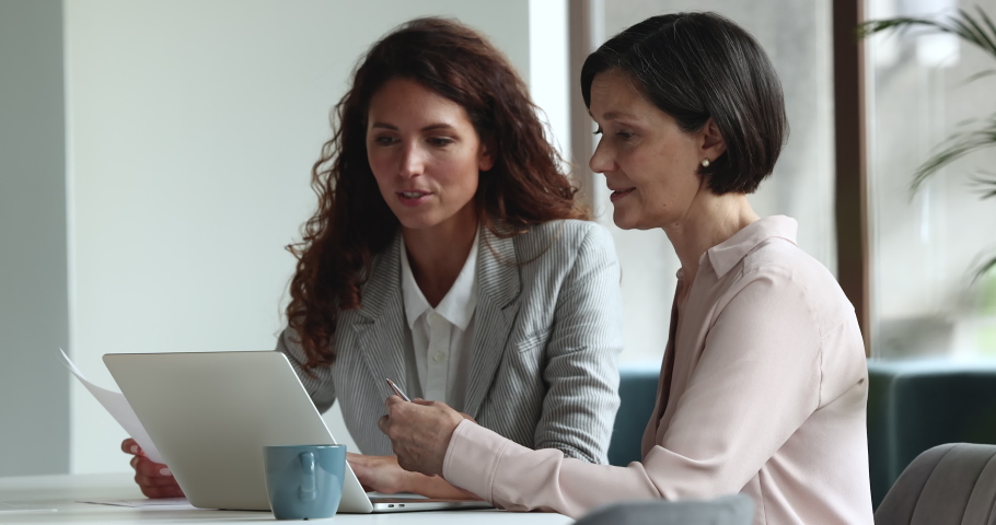 Teamwork, formal meeting with client in company office, consider agreement terms. Hispanic millennial and middle-aged women gather to discuss contract details, planning cooperation, work at workplace Royalty-Free Stock Footage #1097249799