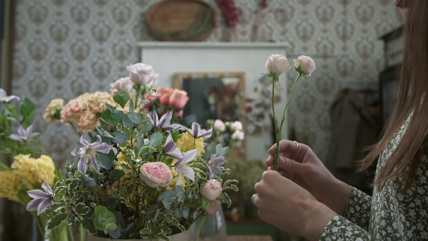 Young woman picking flowers for beautiful bouquet of fresh roses and carnations in basket. Female florist working on nice composition in workshop