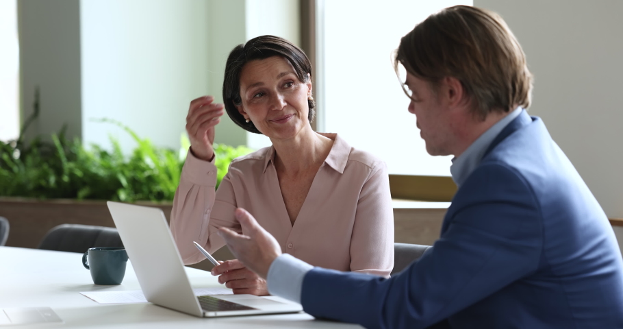 Middle-aged female sales manager provides information, makes presentation on laptop talking to male company client in office. Two employees, workmates discuss new project, software or business app Royalty-Free Stock Footage #1097251351