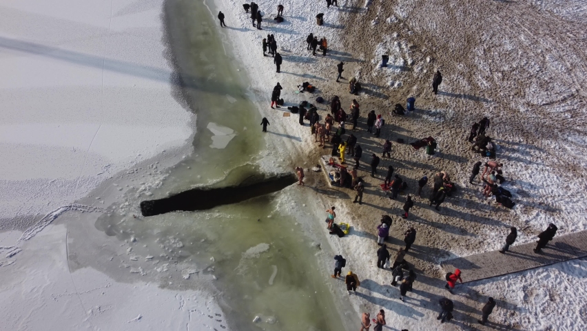 the drone flies over the hole in the winter rake, the river is covered with ice, people enter the cold water, cross themselves and plunge headlong into the ice water three times
