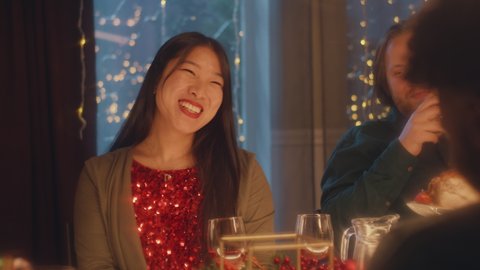 Asian woman drinks wine, talks and smile. Multi cultural friends celebrating Christmas or New Year 2023. Served holiday table. Warm atmosphere of Christmas dinner at home. Christmas party.: film stockowy