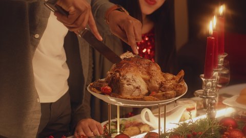 Close-up shot of African American man cutting turkey or chicken. Multi cultural family celebrating Christmas or Thanksgiving Day. Served table with dishes and candles. Family Christmas dinner at home. - Βίντεο στοκ