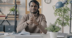 Portrait of Indian man making online video call from office speaking and gesturing using earphones. Business communication and technology concept.