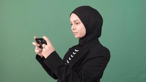 Muslim woman play game phone, young person is very careful looking phone screen in front of green screen, chroma key