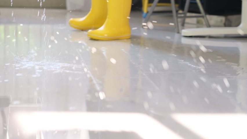 child in yellow boots removes water with a mop. consequence of the flood. Clean water flows on floor covering wooden laminate flooring because of hard pipe damage causing flood in apartment close view Royalty-Free Stock Footage #1097265333