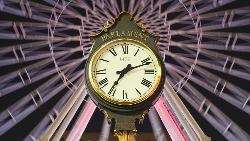 Parliament street clock night timelapse with Christmas ferris wheel in the back.1459, engraved on the clock face, represents the year Romania capital Bucharest was first mentioned in documents.